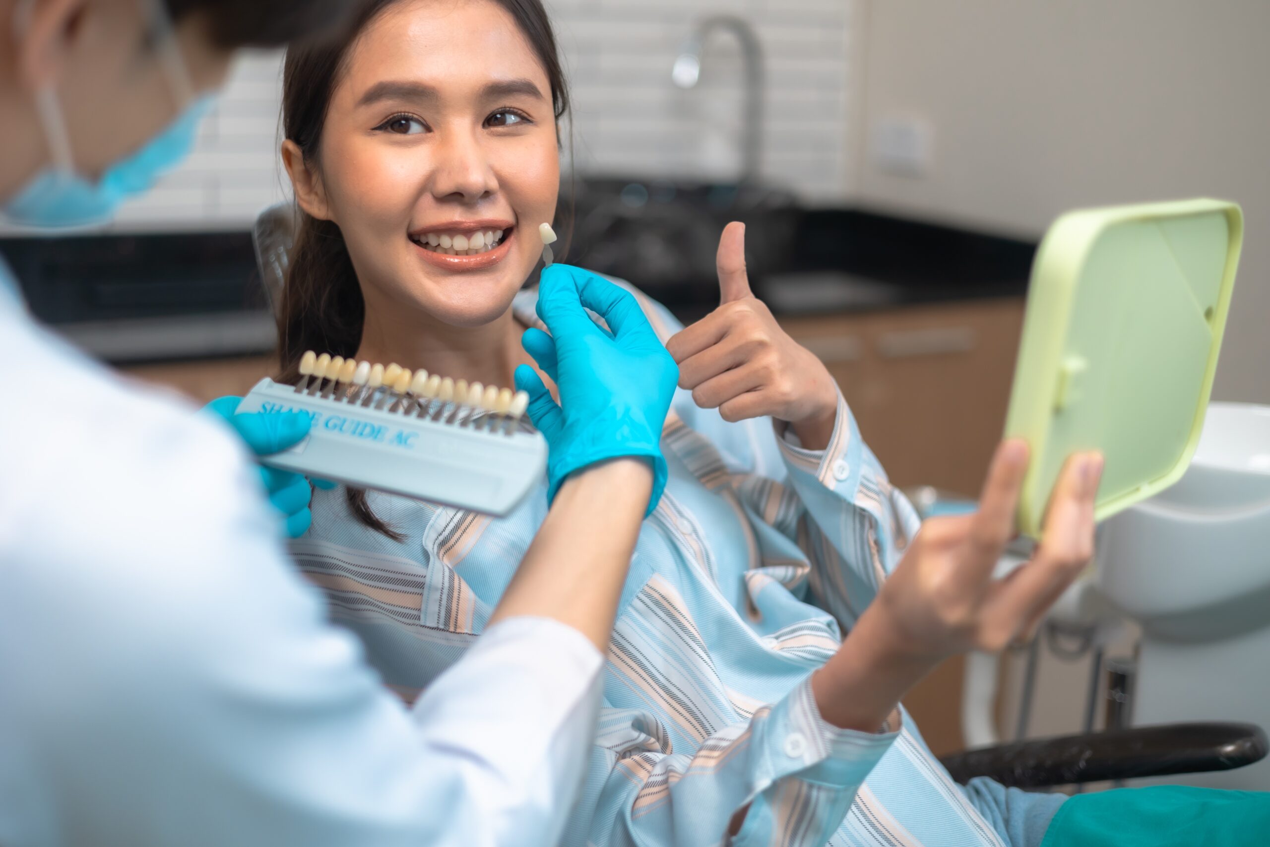 young woman putting a thumbs up and smiling, dentist holding a tray of teeth sample of different shades